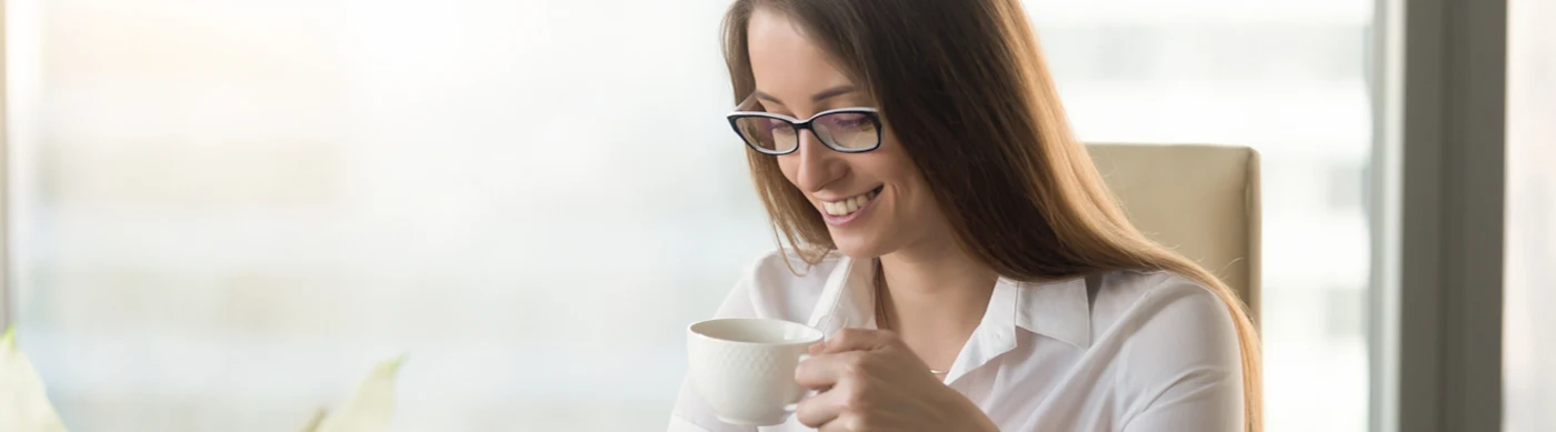 Woman wearing glasses sitting down drinking from a cup.