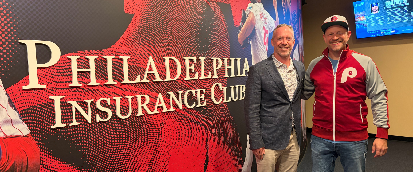 PHLY employee and agent partner stand behind the welcome sign at the Philadelphia Insurance Club premier seating destination located in Citizen's Bank Park
