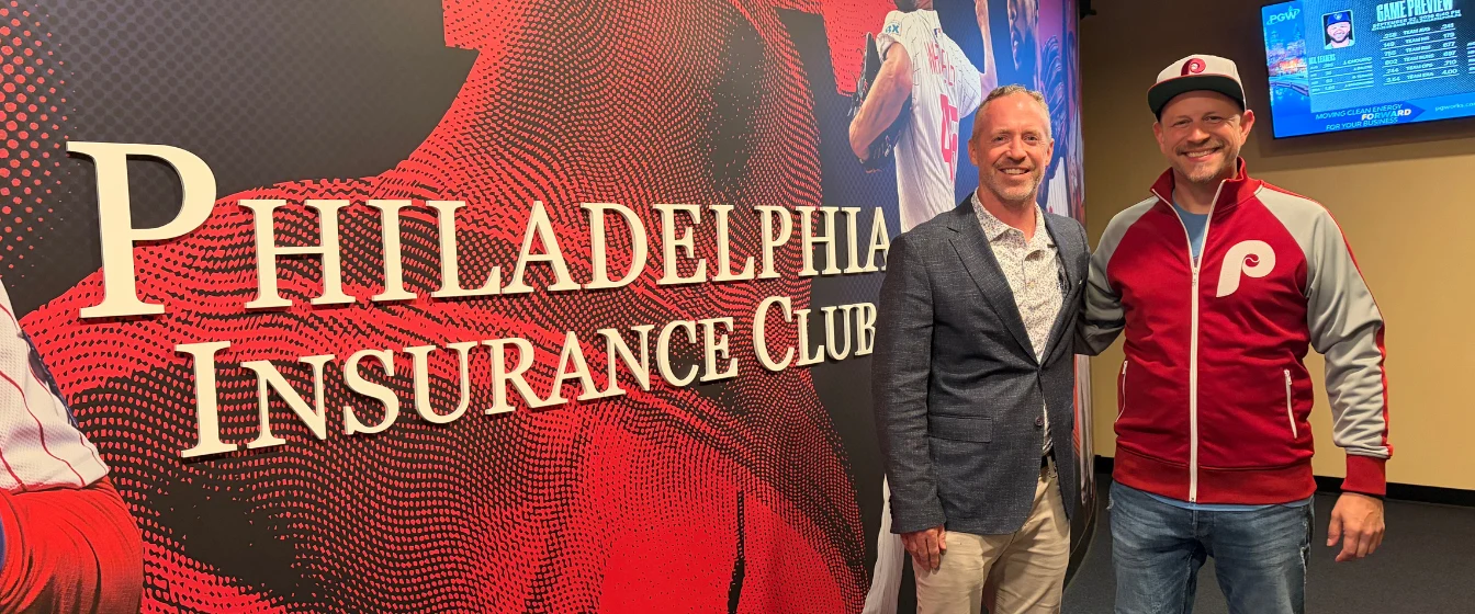 PHLY employee and agent partner stand behind the welcome sign at the Philadelphia Insurance Club premier seating destination located in Citizen's Bank Park