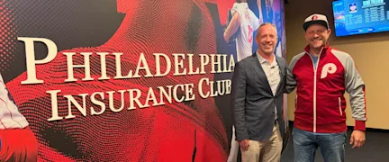 PHLY employee and agent partner stand behind the welcome sign at the Philadelphia Insurance Club premier seating destination located in Citizen's Bank Park