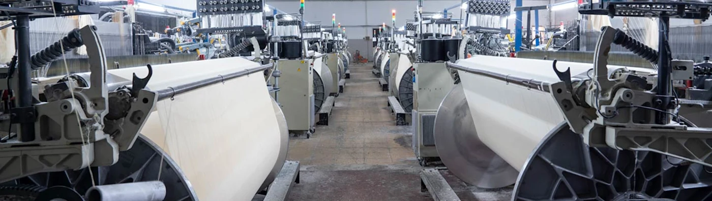 Modern textile manufacturing facility with rows of automated fabric weaving machines and industrial equipment.