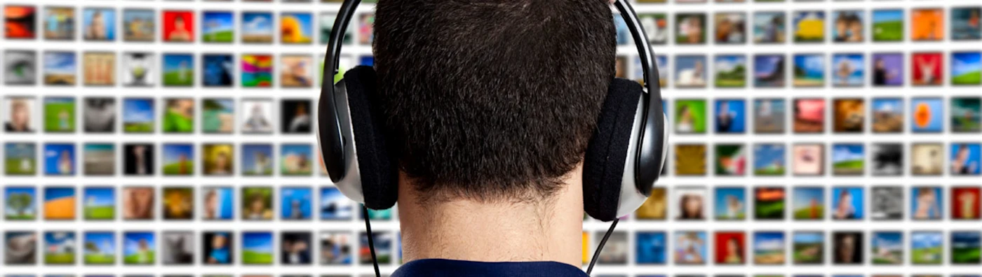 Person wearing headphones viewed from behind, facing a large screen or wall filled with colorful media thumbnails.