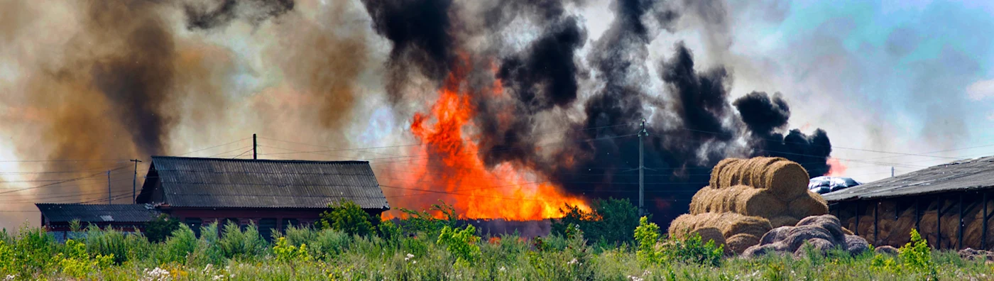A farm on fire with black smoke next to haybales