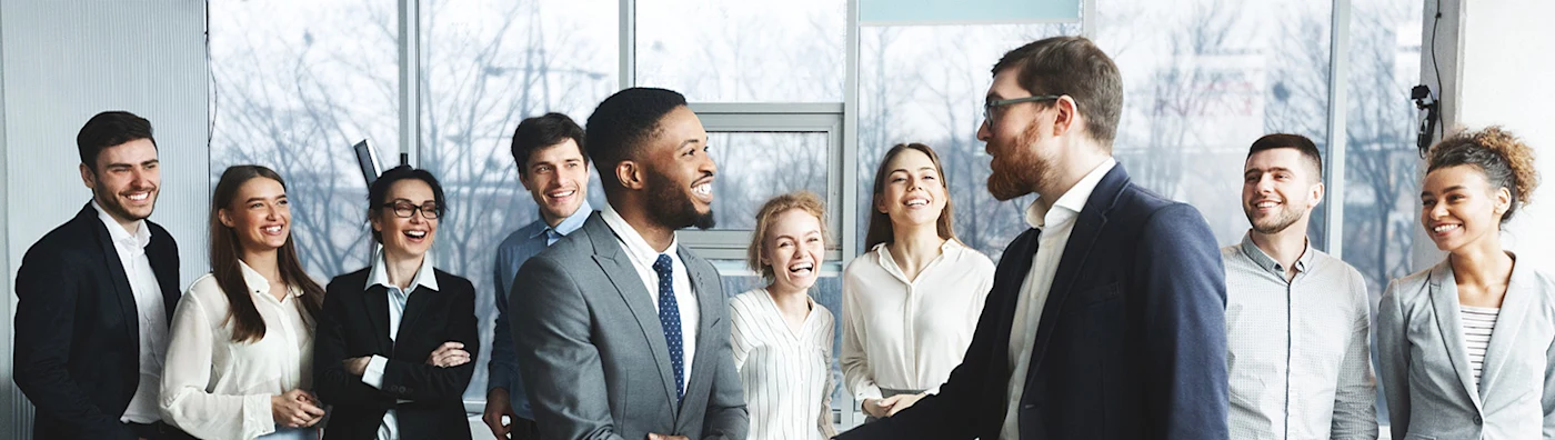 Business team smiling as two colleagues shake hands in a bright, modern office setting.
