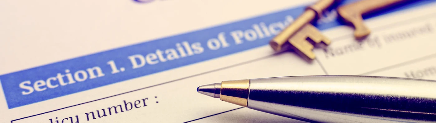 Close up of an insurance policy form with a silver pen and house keys placed on top.