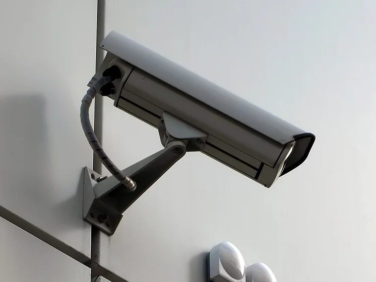 Close up of a mounted security camera on a plain wall angled downward.