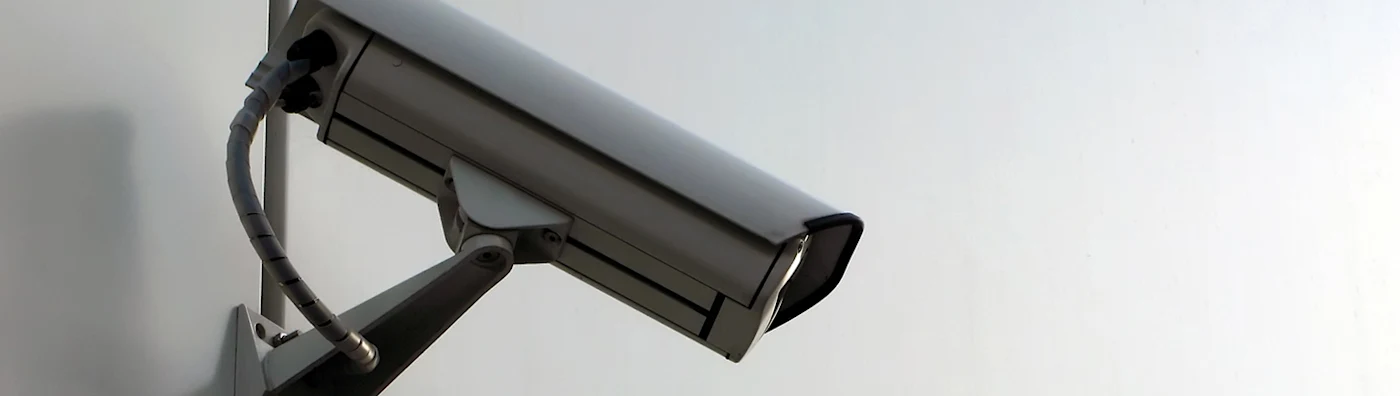 Close up of a mounted security camera on a plain wall angled downward.