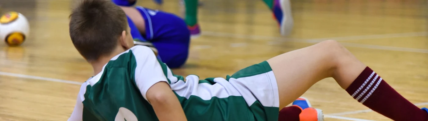 Child in sports uniform lies on indoor court after a fall during a soccer game.