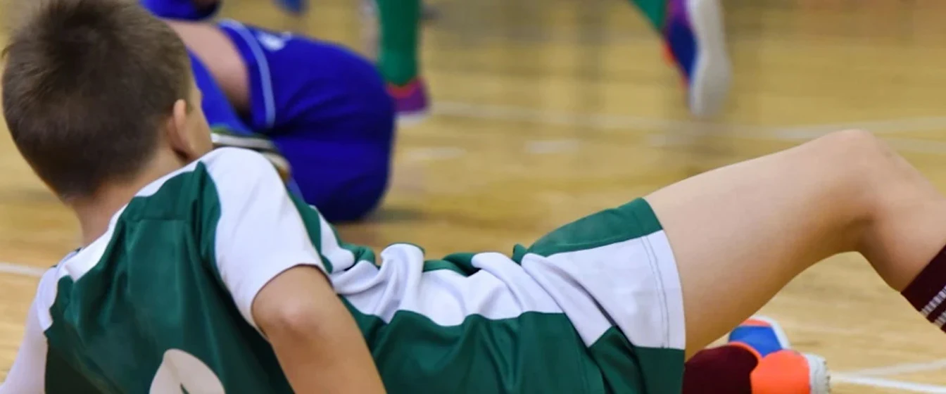 Child in sports uniform lies on indoor court after a fall during a soccer game.
