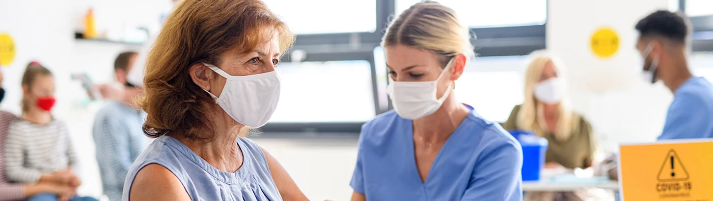 Woman in a mask receives a Covid vaccine at a vaccine clinic from masked nurse