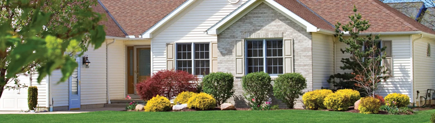 Single-story suburban home with well-maintained lawn, shrubs, and colorful landscaping in front.