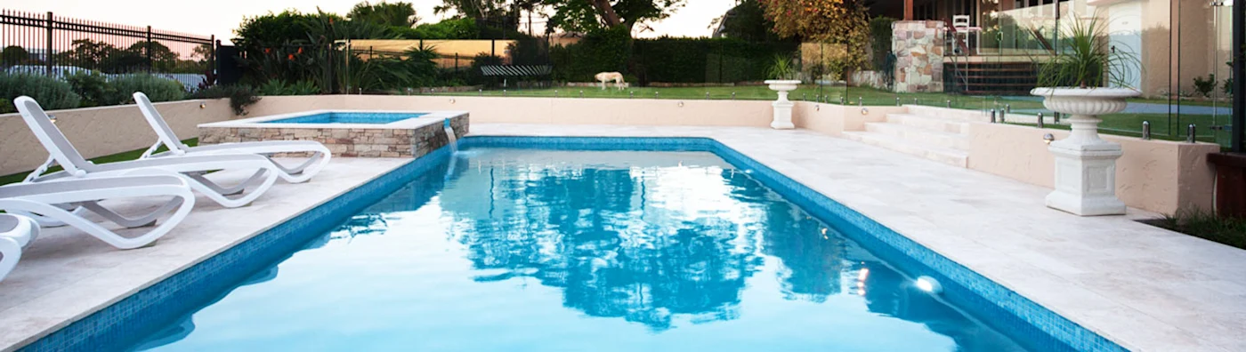 Swimming pool with lounge chairs, hot tub, and surrounding landscaping.