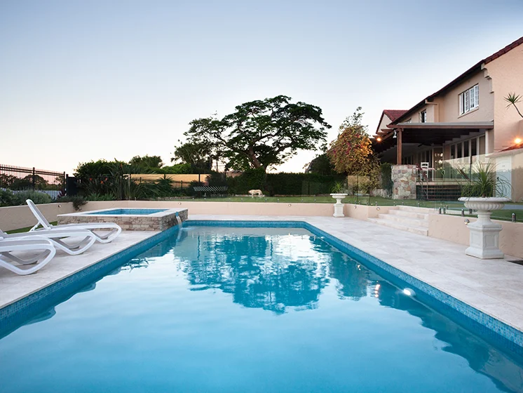 Swimming pool with lounge chairs, hot tub, and surrounding landscaping.