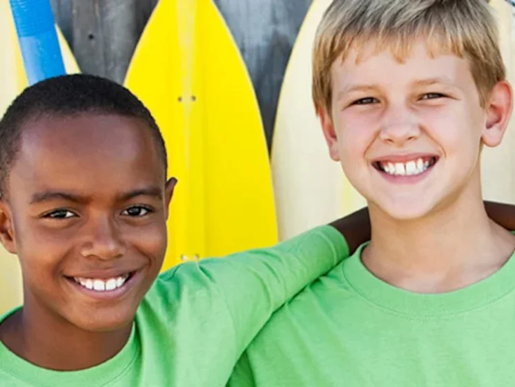Two kids in front of row of yellow surf boards
