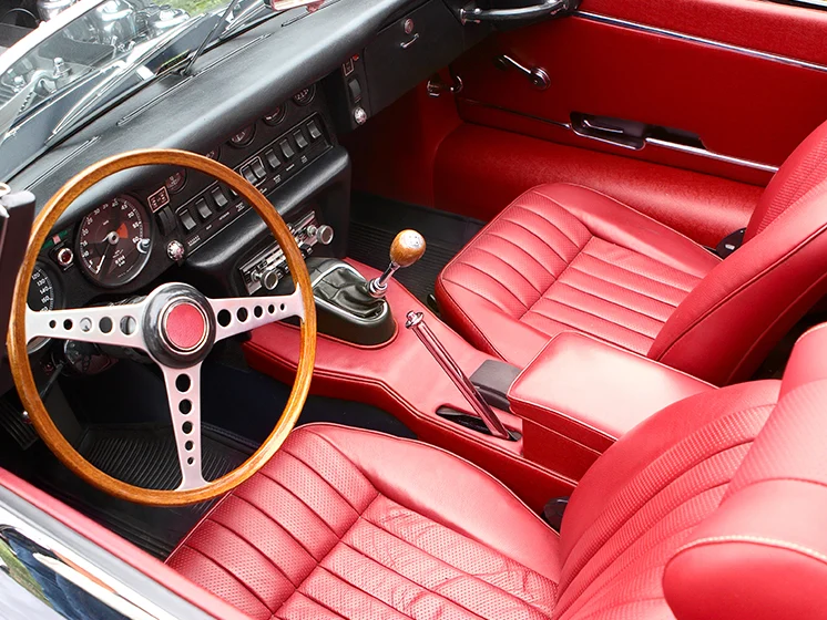 Close up image of the interior of an antique vehicle with red leather seats, a wood steering wheel, and manual gear shift.