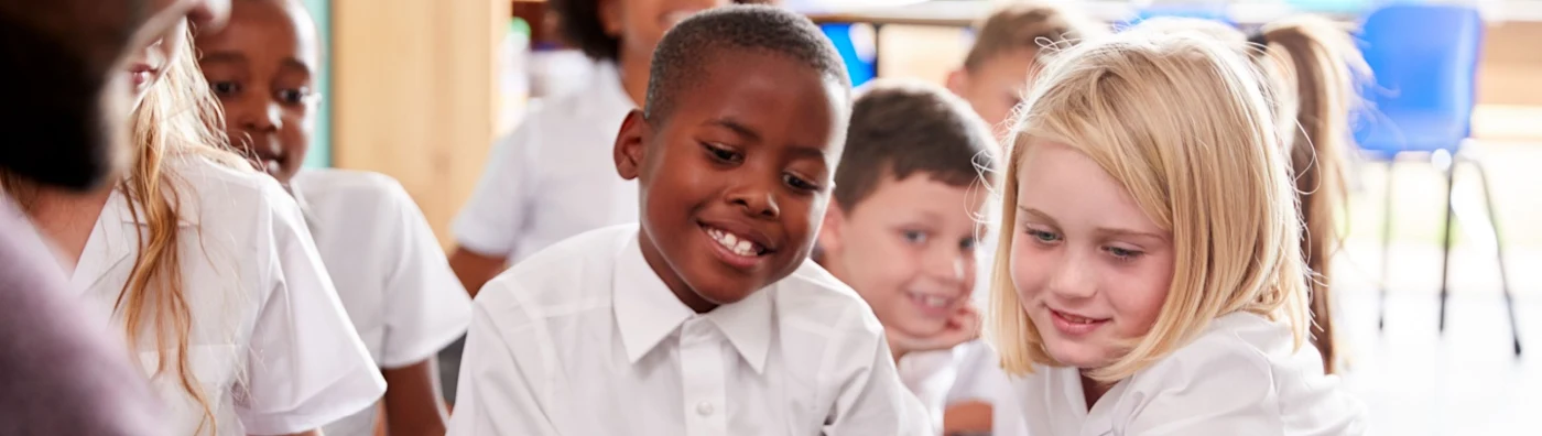 Group of young children in school uniforms smiling and engaging in a classroom activity.