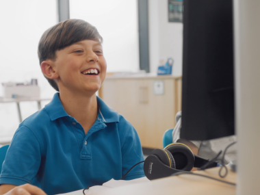 A young boy sits in an Explore Learning centre smiling as he sits at a desk in front of a computer.