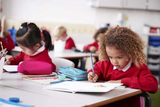 Young girl sitting in class and writing next to her favourite pencil case