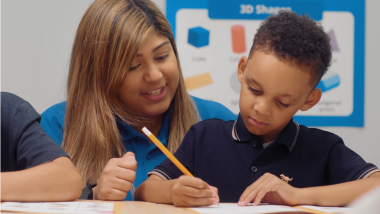 A young child is writing in a workbook with the support of an Explore Learning tutor.