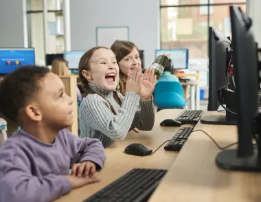 Three children sit at a desk learning on computers.