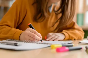 a teenage girl wearing an orange jumper highlighting passages in a notebook.