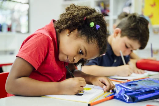 Young girl writing in a class with her pencil case in front of her