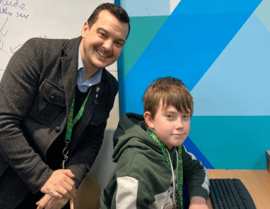 Centre Director, Sean, with an Explore Learning member at a computer, both are wearing a sunflower lanyard, which is a symbol for people to showcase that they have a hidden disability. 