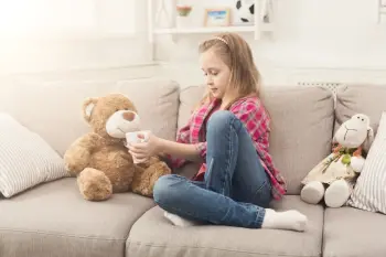 beautiful little girl on a sofa treating her teddy bear with tea