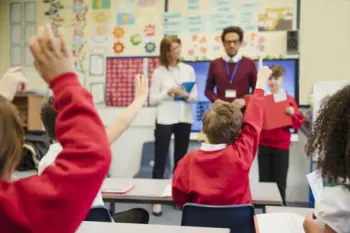 Children in school with teachers putting their hands up