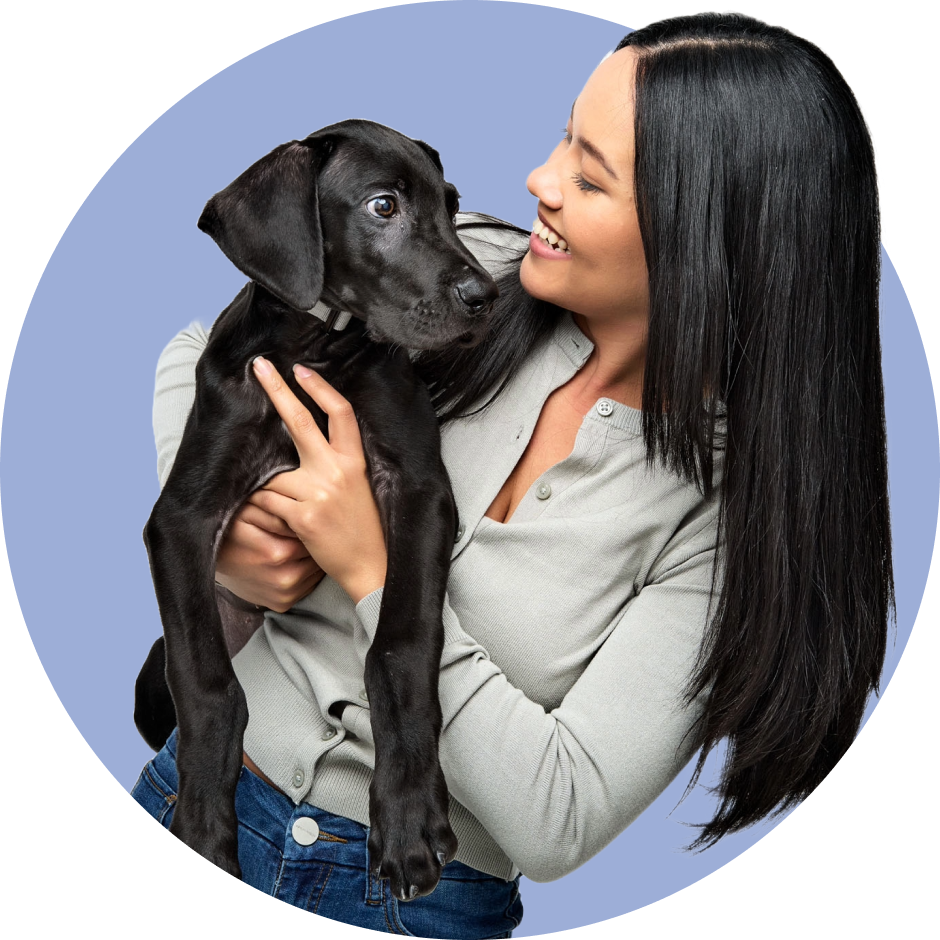 A woman embraces her furry companion, a black dog, with a smile on her face.