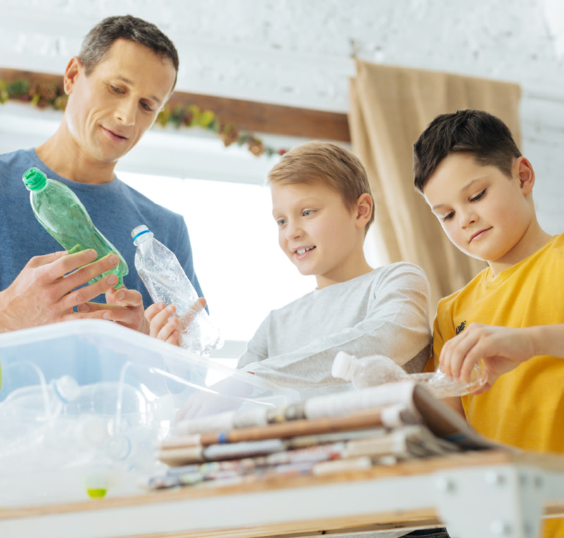 A father showing two young boys how to recycle plastic