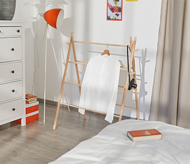 A white shirt hung out to dry on a wooden dryer in a bedroom