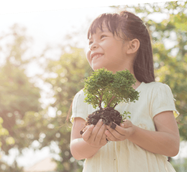 A young girl smiling while holding a bonsai tree in her hands