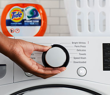 A hand setting the program on a white washing machine
