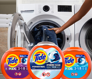 A range of Tide PODS products in front of a washing machine being loaded