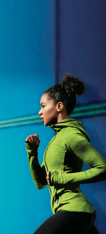 A young woman in a green sports top and black sports pants running in front of a blue background