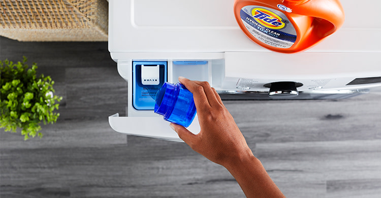 A person pouring Tide liquid detergent into the detergent dispenser