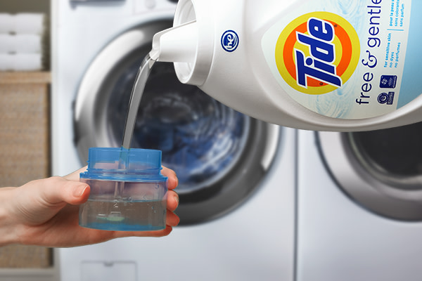 A person pouring Tide liquid detergent into a measurement cup