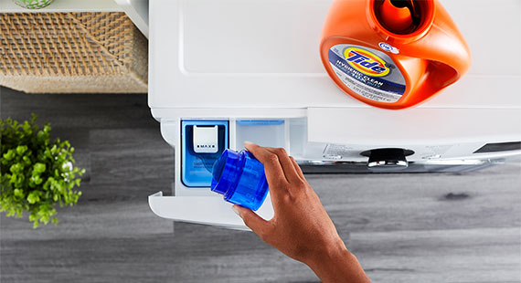 A hand pouring Tide liquid laundry detergent in the dispenser drawer of a washing machine