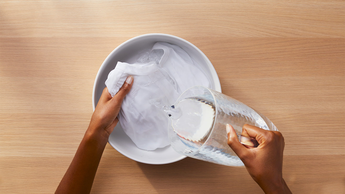 A person rinsing a white garment with cold water