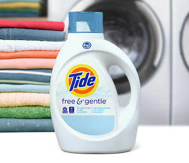 A white bottle of Tide Free and Gentle liquid laundry detergent in front of colorful folded clothes and a washing machine