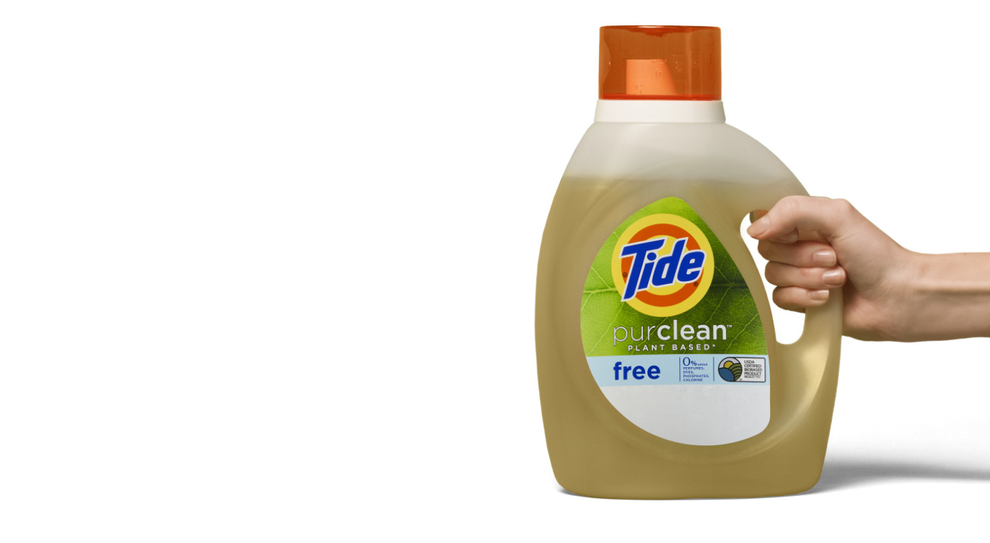 A hand holding a bottle of Tide Tide purclean™ plant-based liquid laundry detergent