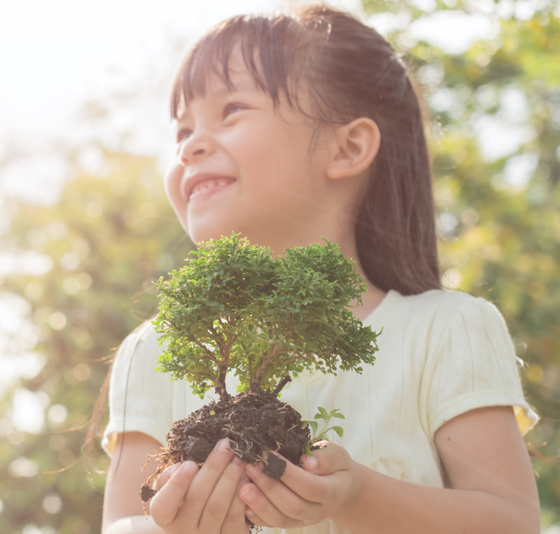 A young girl smiling while holding a bonsai tree in her hands
