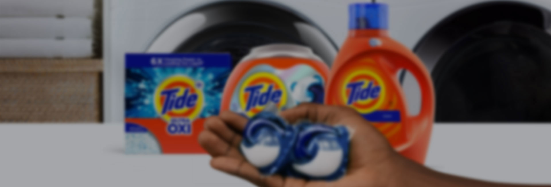 A person holding Tide PODS  washing capsules in front of some Tide laundry products