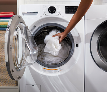 A white front-loading washing machine being loaded with white clothes