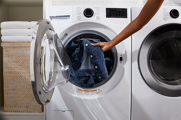A person is loading denim garments into the washing machine drum