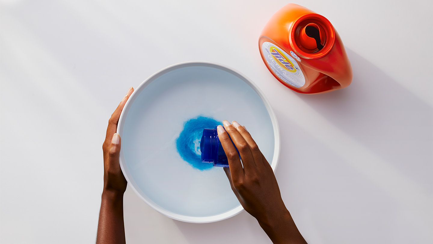 A person pouring Tide liquid detergent into a bowl of water