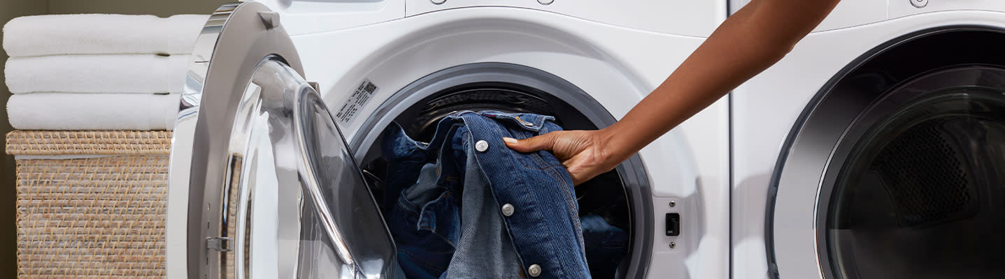 A person loading a denim jacket into the drum