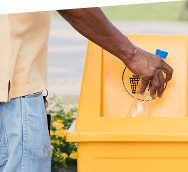 A man putting a plastic bottle in a yellow recycling bin