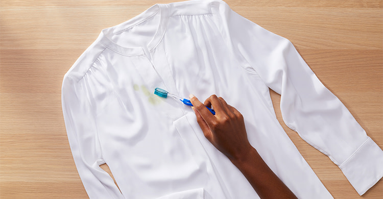A person removing excess stain from a white shirt with a toothbrush